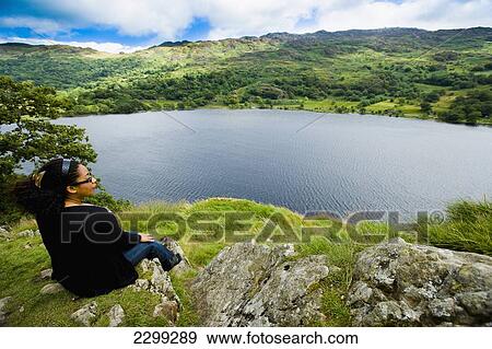 Stock Photo - UK, North Wales, Snowdonia National Park, Nantgwynant, from a rocky outcrop; Llyn Gwynant Campsite, glistening in the sunlight. women sitting down enjoying the view over the lake, Lake Nant Gwynant. Fotosearch
