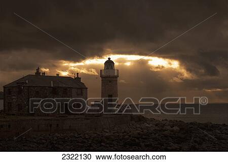 Stock Image - UK, Scotland, Dumfries and Galloway, Portpatrick, Lighthouse on shore and dark storm clouds. Fotosearch