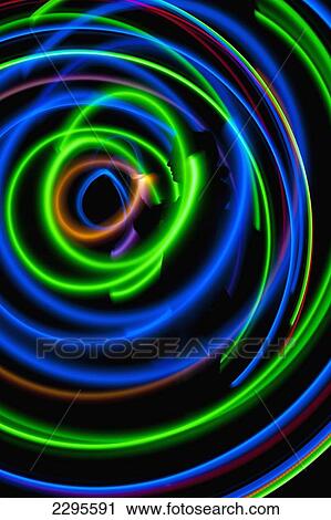 Stock Image - UK, Silhouette of woman spinning hula-hoop lit with LEDs in field at night; West Sussex. Fotosearch