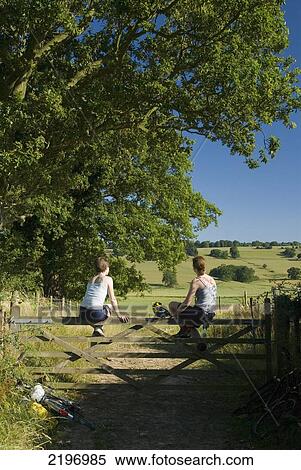 Stock Photography - UK, Two cyclists resting on gate on bridleway near Winchelsea; East Sussex. Fotosearch
