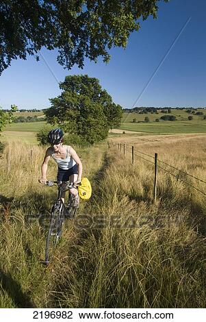 Stock Image - UK, Woman cycling up bridleway near Winchelsea; East Sussex. Fotosearch