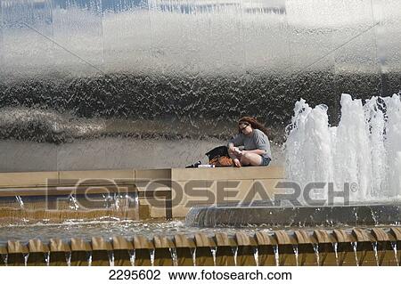 Stock Image - UK, Woman reading book beside fountains outside Sheffield train station; South Yorkshire. Fotosearch