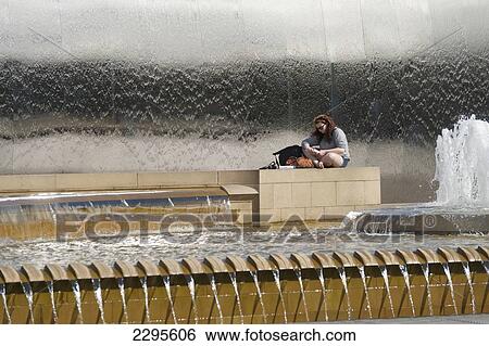 Stock Photograph - UK, Woman reading book beside fountains outside Sheffield train station; South Yorkshire. Fotosearch