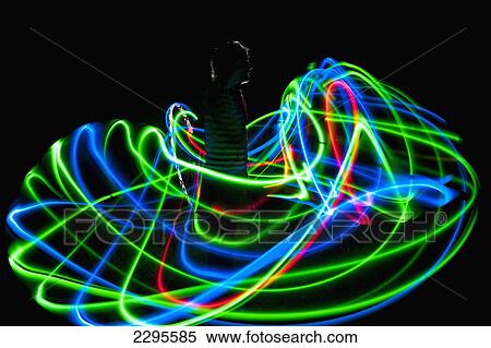 Stock Photography - UK, Woman spinning hula-hoop lit with LEDs in field at night; West Sussex. Fotosearch