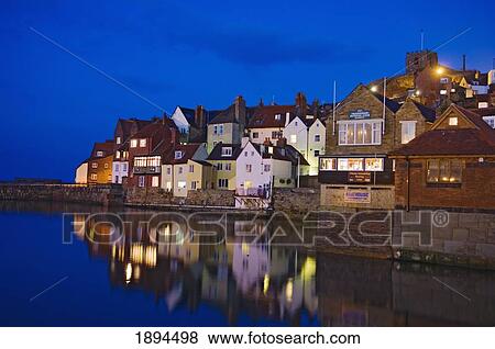 Stock Photo - UK, Yorkshire, Houses reflecting in water at dusk; Whitby. Fotosearch