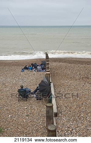 United Kingdom, England, East Sussex, grey summers day; Eastbourne, Tourists sitting on Eastbourne beach on an overcast View Large Photo Image Picture - United Kingdom, England, East Sussex, grey summers day; Eastbourne, Tourists sitting on Eastbourne beach on an overcast. Fotosearch