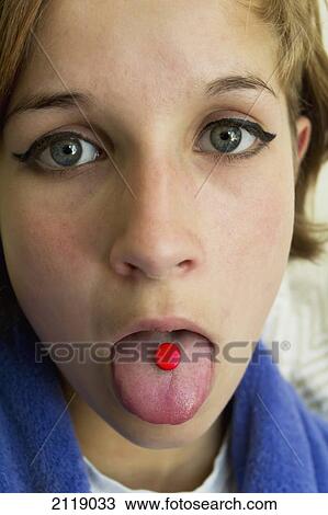 Stock Image - United Kingdom, England, Esher, Teenager with red tablet medicine. Fotosearch