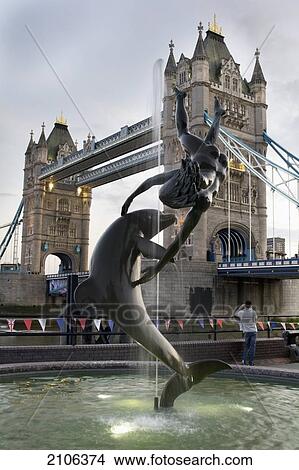 Picture - United Kingdom, Girl with Dolphin statue in front of Tower Bridge; London. Fotosearch