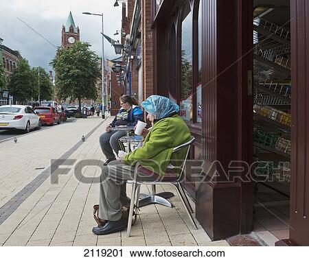Stock Image - United Kingdom, Northern Ireland, County Londonderry, Old woman wearing hair net outside cafe; Derry. Fotosearch