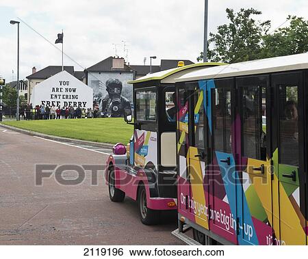 Stock Photograph - United Kingdom, Northern Ireland, County Londonderry, Tourist land train passing gallery murals in Rossville Street in Bogside Area; Derry. Fotosearch