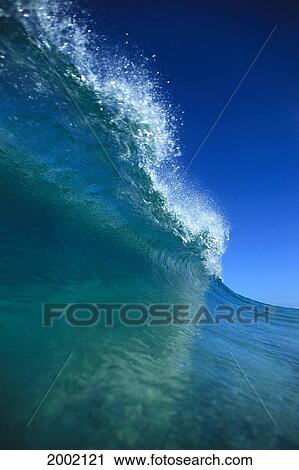 Stock Image - Upward View Of Large Turquoise Wave, Spray At Lip, Blue Sky Above. Fotosearch