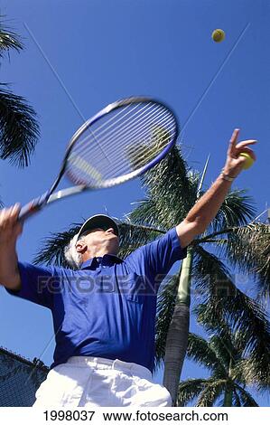 Stock Photo - Upward View Of Senior Man Playing Tennis, Palm Trees And Blue Sky A07E. Fotosearch