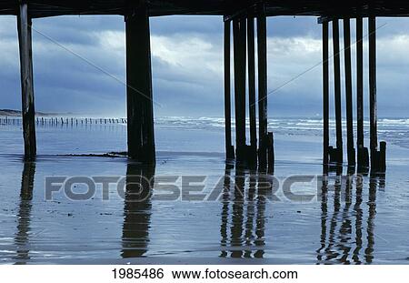 Stock Photograph - USA, California, Reflections on wet shoreline framed by silhouetted pier; Pismo Beach. Fotosearch