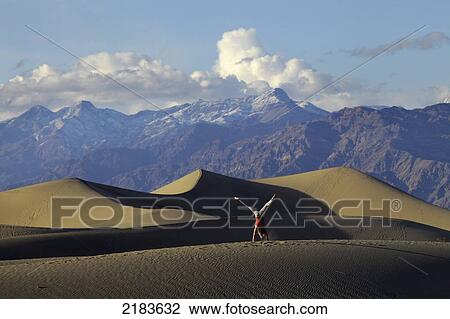 Stock Image - Usa, California, Young Woman Doing Cartwheel On Mesquite Flat Sand Dunes With Amargosa Range Mountains In Background; Death Valley National Park. Fotosearch