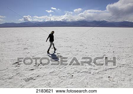 Stock Image - Usa, California, Young Woman Walking Across Badwater Salt Flats; Death Valley National Park. Fotosearch