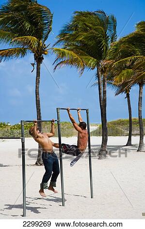 Stock Photo - USA., Florida, Miami, doing pull ups on metal bars; South Beach, Two men working out at the beach. Fotosearch