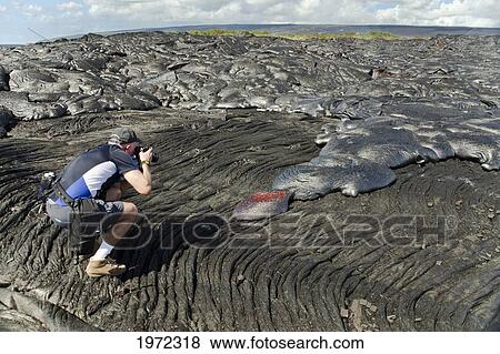 Stock Photo - USA, Hawaii Islands, Big Island, Man Photographs Pahoehoe Lava Flowing From Kilauea Covering Older Pahoehoe Flow; Kalapana. Fotosearch