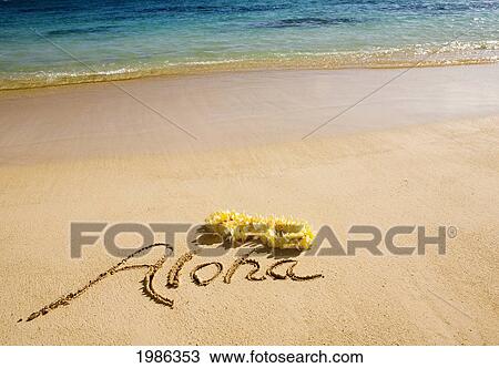 Stock Image - USA, Hawaii Islands, Oahu, Aloha written in sand with yellow Plumeria Lei and Turquoise ocean; Lanikai Beach. Fotosearch