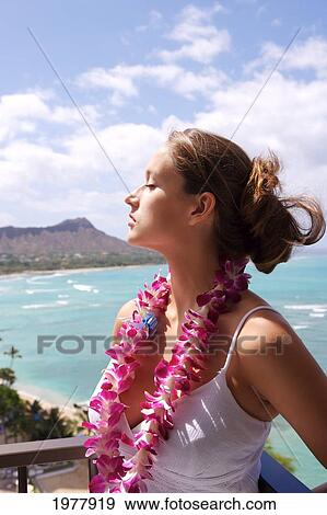 Stock Photo - USA, Hawaii, Oahu, Diamond Head in background; Waikiki, Beautiful woman with eyes closed wearing Orchid Lei. Fotosearch