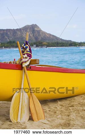 Stock Image - USA, Hawaii, Oahu, Honololu, funeral for Don Ho; Waikiki, Canoe paddles and Lei leaning on outrigger canoe. Fotosearch