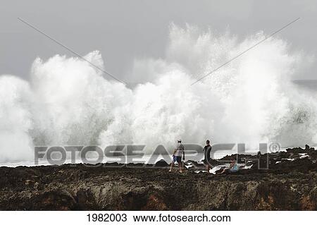Stock Image - USA, Hawaii, Oahu, people watching; North Shore, Wave crashing against shore of Pacific ocean. Fotosearch