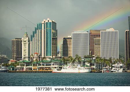 Stock Image - USA, Hawaii, Oahu, Rainbow over downtown and harbor; Honolulu. Fotosearch