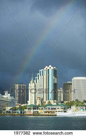 Stock Image - USA, Hawaii, Oahu, Rainbow over downtown and harbor; Honolulu. Fotosearch