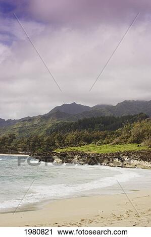 Stock Image - USA, Hawaii, Oahu, Scenic landscape with sandy beach of Pacific Ocean and mountain; Windward. Fotosearch