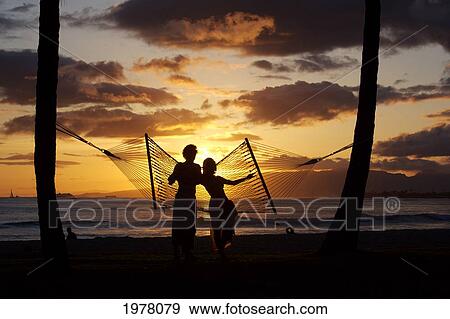 Stock Photo - USA, Hawaii, Oahu, Silhouette of woman and man standing by hammock in Kapiolani Park; Waikiki. Fotosearch