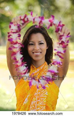 Stock Photograph - USA, Hawaii, Portrait of woman wearing yellow pareo and holding out lei; Oahu. Fotosearch