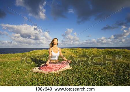 Stock Photo - USA, Hawaii, Young woman doing yoga on grassy hill near Pacific Ocean; Maui. Fotosearch