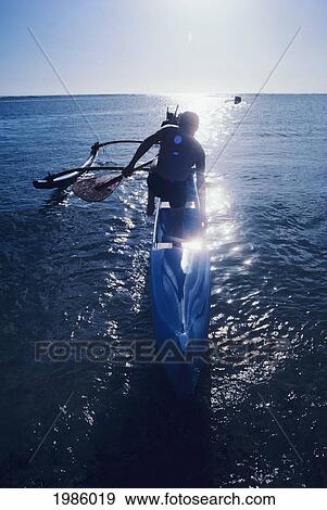USA, Man standing in outrigger canoe with paddle on shimmering ocean; Hawaii Islands View Large Photo Image Stock Photo - USA, Man standing in outrigger canoe with paddle on shimmering ocean; Hawaii Islands. Fotosearch