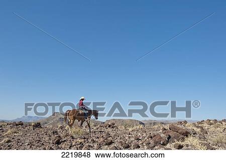 Stock Photo - USA, Men horseback riding among desert landscape; Texas. Fotosearch