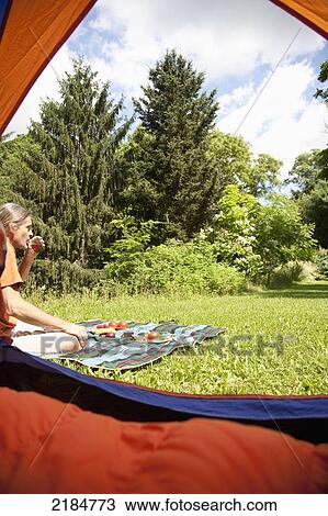 Stock Image - Usa, New York State, Man Drinking While Sitting In Front Of Tent At Camping Site; Hudson Valley. Fotosearch