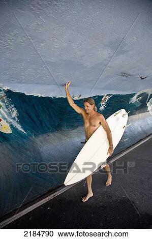 Stock Image - Usa, New York State, Man Walking With Surfboard By Wall Depicting High Wave; Rockaway. Fotosearch