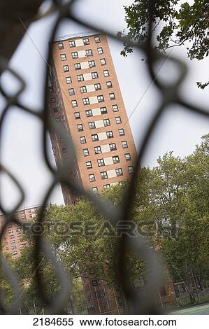 Stock Photography - Usa, New York State, New York City, Apartment Building Seen Through Chainlink Fence; Harlem. Fotosearch