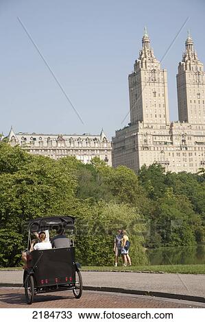 Stock Image - Usa, New York State, Tourists In Pedicab Overlooking Water In Central Park; New York City. Fotosearch