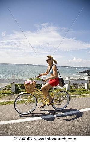 Stock Image - Usa, Rhode Island, Young Woman Bicycling Along Ocean Avenue; Newport. Fotosearch