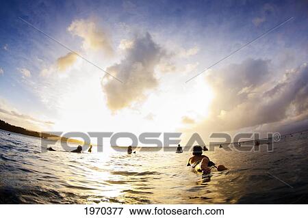 Stock Photo - USA, Surfers Float On Surfboards At Sunset; Hawaii Islands. Fotosearch