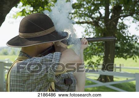 Stock Photograph - USA, Virginia, A man wearing period costume fires a musket gun. Ash Lawn-Highland. Home of the 5th president. James Monroe; Charlottesville. Fotosearch