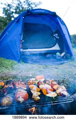 Picture - Vegetable Kebab Skewers Grilling On Campfire With Tent In Background. Fotosearch