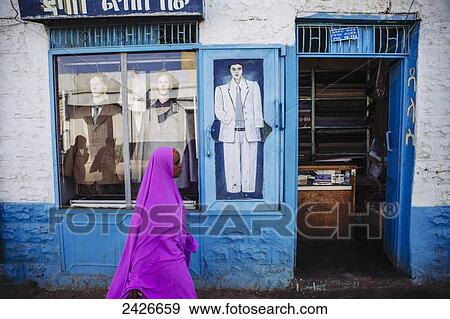 Stock Photo - Veiled woman in pink walks past a tailors shop in the old city of Harar in Eastern Ethiopia; Harar, Ethiopia. Fotosearch