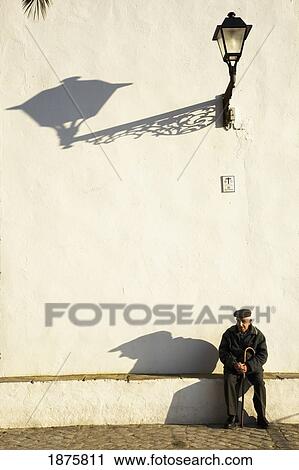 Stock Image - Vejer De La Frontera, Andalusia, Spain; An Elderly Man Sitting Against A White Building. Fotosearch