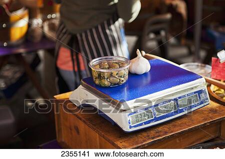 Stock Image - Vendor weighing food on a food scale at Portobello Market; London, England. Fotosearch