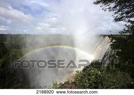Stock Image - Victoria Falls with a rainbow in the mist; Zambia. Fotosearch