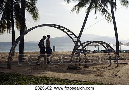 Stock Image - Vietnam, Travelers Walking Past A Climbing Frame; Nha Trang. Fotosearch