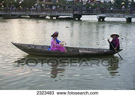 Stock Image - Vietnam, Vietnamese Couple In Traditional Dress In Boat; Hoi An. Fotosearch