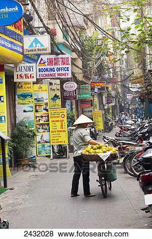 Stock Photo - Vietnamese woman with oranges on her bicycle, Hanoi street scene in the French Quarter; Hanoi, Vietnam. Fotosearch