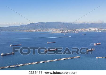 Stock Photo - View Across Gibraltar Bay, Also Known As Algeciras Bay, To Algeciras In Spain With Cargo Boats At Anchor In Gibraltarian Waters And The Ceuta To Algeciras Ferry Behind Cargo Boats; Gibraltar. Fotosearch