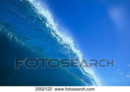 Stock Image - View From Below Of Large Blue Wave, Spray At Lip, Blue Sky Beyond. Fotosearch